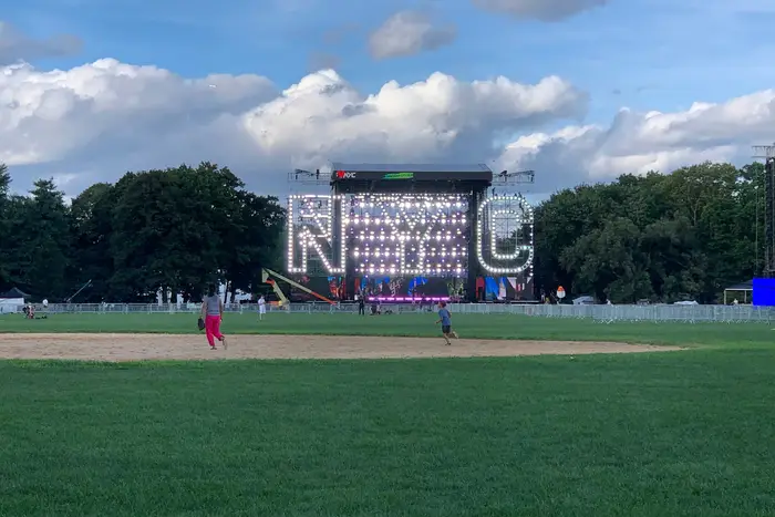 The "N-Y-C" backdrop for the Homecoming concert in Central Park's Great Lawn, with kids playing baseball in a field in the foreground